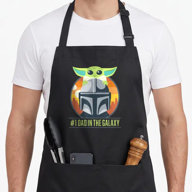 Tablier de cuisine noir avec illustration de Grogu et du casque Mandalorian sous le texte #1 DAD IN THE GALAXY