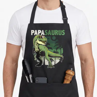 Tablier de cuisine noir avec un T Rex vert aux lunettes de soleil et le mot Papasaurus