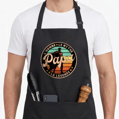 Tablier de cuisine noir avec un logo circulaire vintage affichant Papa l'homme le mythe la légende et une silhouette de super-héros.