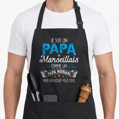 Tablier de cuisine noir avec l'inscription Je suis un papa marseillais comme un papa normal mais beaucoup plus cool en bleu et blanc.