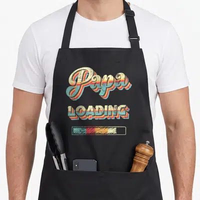 Tablier de cuisine noir avec typographie retro Papa Loading et une barre de chargement colorée.