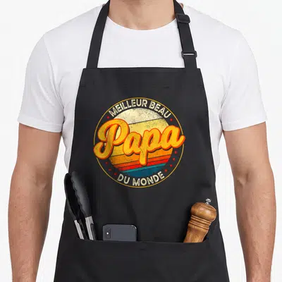Tablier de cuisine noir avec un logo circulaire retro affichant Papa Meilleur Beau Du Monde entouré d'étoiles rouges.