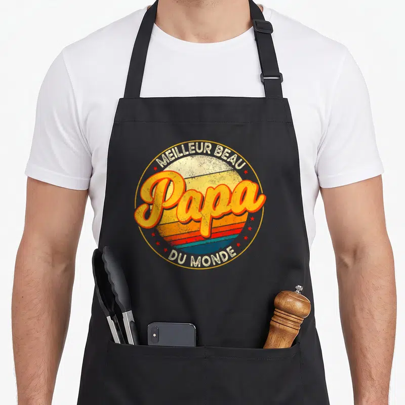 Tablier de cuisine noir avec un logo circulaire retro affichant Papa Meilleur Beau Du Monde entouré d'étoiles rouges.