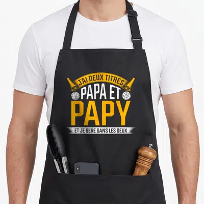 Tablier de cuisine noir avec inscription jaune et blanche J'ai deux titres papa et papy et je gere dans les deux.
