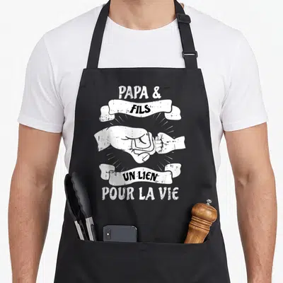 Tablier de cuisine noir avec illustration blanche de deux poings se touchant et des banderoles textuelles.