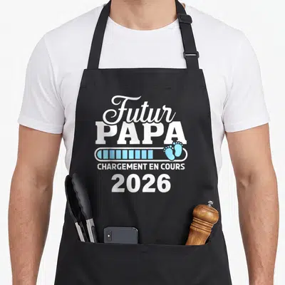 Tablier de cuisine noir avec inscription Futur Papa chargement en cours 2026 et empreintes de pieds bleues.