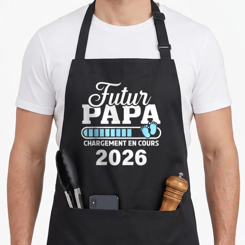 Tablier de cuisine noir avec inscription Futur Papa chargement en cours 2026 et empreintes de pieds bleues.