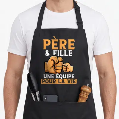 Tablier de cuisine noir avec illustration de poings se touchant et texte Père et Fille Une équipe pour la vie en orange et blanc.