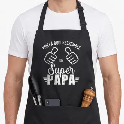 Tablier de cuisine noir avec deux mains faisant des pouces levés et le texte voici à quoi ressemble un super papa en blanc.