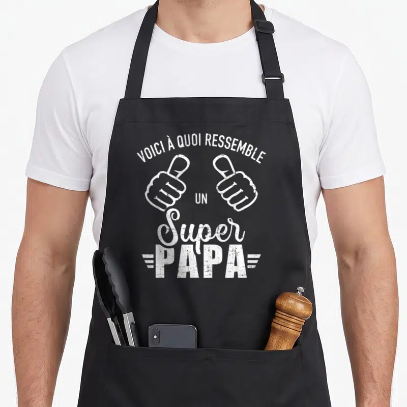 Tablier de cuisine noir avec deux mains faisant des pouces levés et le texte voici à quoi ressemble un super papa en blanc.