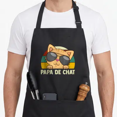 Tablier de cuisine noir avec un chat orange aux lunettes noires et l'inscription Papa De Chat sur fond arc-en-ciel vintage.