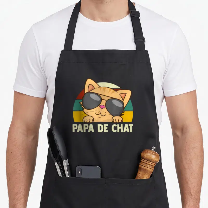 Tablier de cuisine noir avec un chat orange aux lunettes noires et l'inscription Papa De Chat sur fond arc-en-ciel vintage.