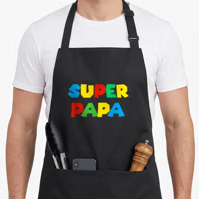 Tablier de cuisine noir avec l'inscription Super Papa en lettres pixelisées bleues, jaunes, rouges et vertes.