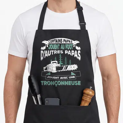Tablier de cuisine noir avec illustration de tronçonneuse et texte humoristique sur les papas bûcherons.