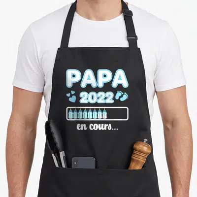 Tablier de cuisine noir avec l'inscription Papa 2022 en cours et une rangée de biberons bleus sous la mention chargement en cours.