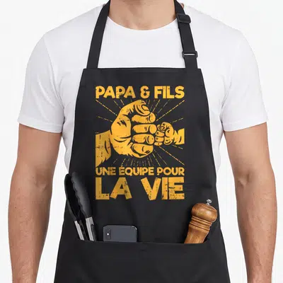 Tablier de cuisine noir avec deux poings orange se serrent et le texte Papa et Fils une equipe pour la vie.