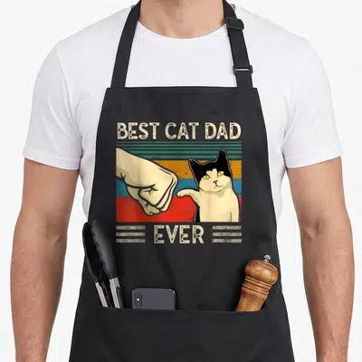 Tablier de cuisine noir avec illustration vintage d'un chat noir et blanc effectuant un high five sur fond de bandes colorées.