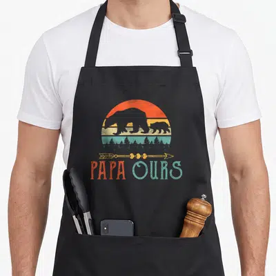 Tablier de cuisine noir avec illustration vintage Papa Ours, silhouettes d'ours et flèche décorative sur fond coloré.