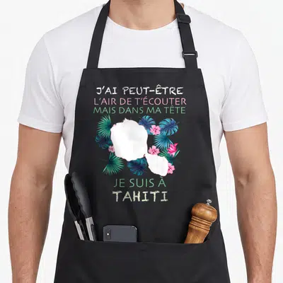 Tablier de cuisine noir avec texte humoristique et illustration de feuilles vertes et fleurs roses tropicales.