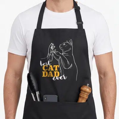 Tablier de cuisine noir avec illustration d'un chat effectuant un high five et du texte bilingue blanc et orange.