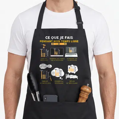 Tablier de cuisine noir avec illustration humoristique sur le bricolage et des outils comme un marteau ou une perceuse.
