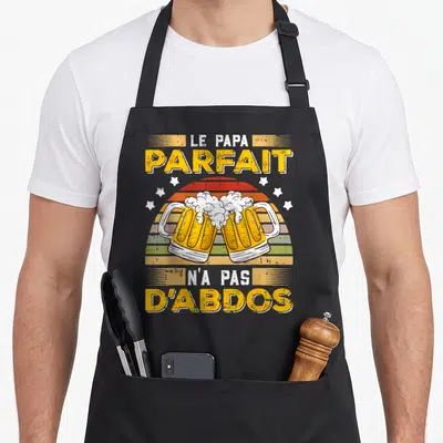 Tablier de cuisine noir avec deux verres de bière se touchant et le texte Le Papa Parfait N'a Pas D'Abdos en jaune et blanc.