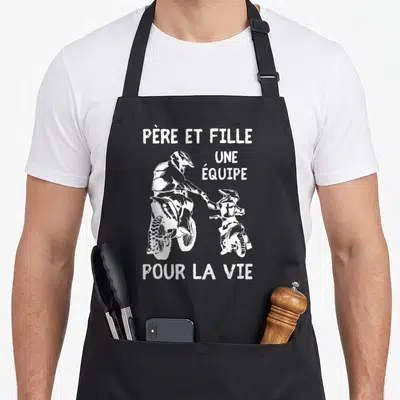 Tablier de cuisine noir avec illustration blanche d'un père et une fille en tenue de motocross se tenant la main.