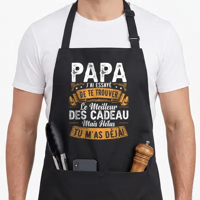 Tablier de cuisine noir avec inscription blanche et bannière orange disant Papa j'ai essayé de te trouver le meilleur des cadeaux mais hélas tu m'as déjà.