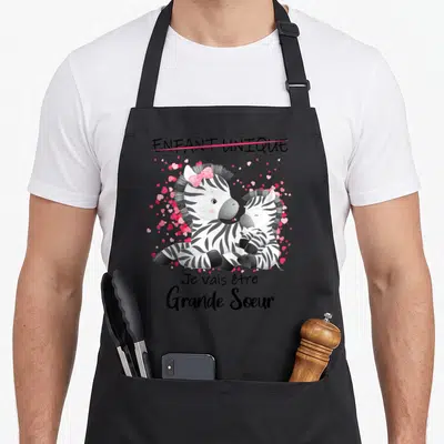 Tablier de cuisine noir avec deux zèbres et le texte Je vais être Grande Soeur entouré de cœurs roses.