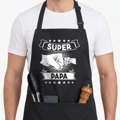 Tablier de cuisine noir avec illustration blanche poings serrés et texte super papa encadré d'étoiles.