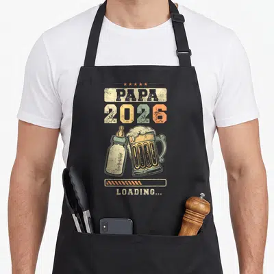 Tablier de cuisine noir avec illustration d'un biberon et d'une bière sous l'inscription Papa 2026 Loading.