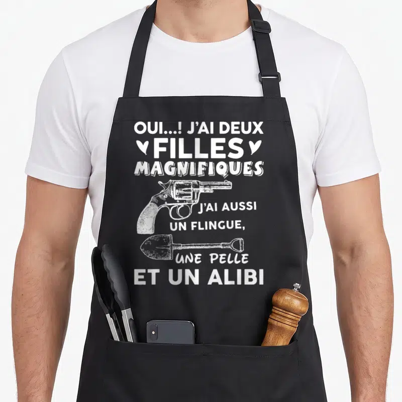 Tablier de cuisine noir avec inscription blanche J'ai deux filles magnifiques illustré d'un revolver et d'une pelle.