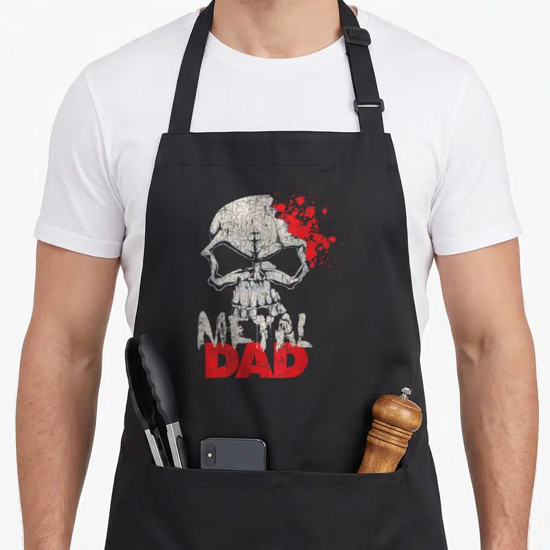 Tablier de cuisine noir avec illustration de crâne blanc et texte Metal Dad en rouge vif.
