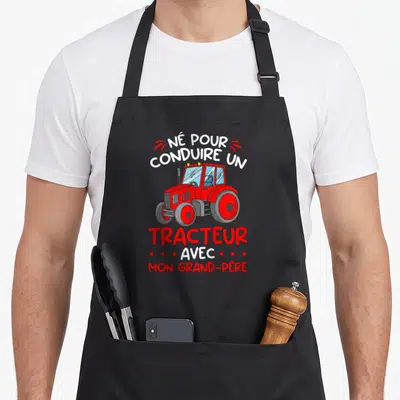 Tablier de cuisine noir avec illustration d'un tracteur rouge et texte blanc et rouge sur fond uni.