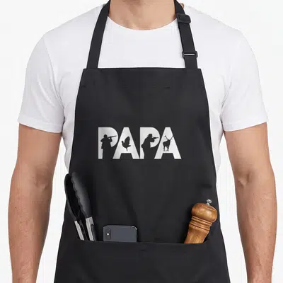 Tablier de cuisine noir avec le mot Papa en blanc intégrant des silhouettes de chasseurs, d'un cerf et d'un gibier d'eau.