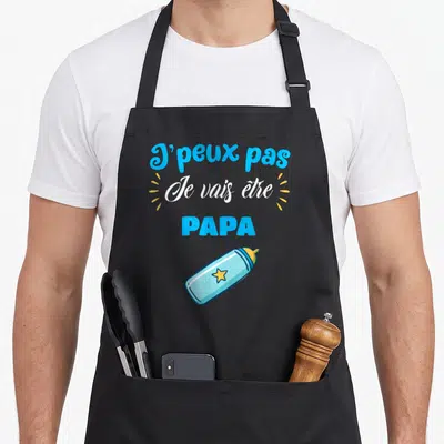 Tablier de cuisine noir avec inscription J'peux pas Je vais être PAPA et illustration de biberon bleu à étoile jaune.