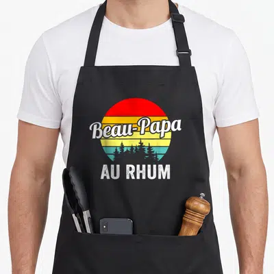 Tablier de cuisine noir avec un soleil vintage multicolore et les mots Beau-Papa au rhum en blanc.