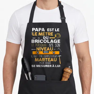 Tablier de cuisine noir avec texte blanc et jaune Papa est le mètre du bricolage entouré d'un marteau et d'un niveau.