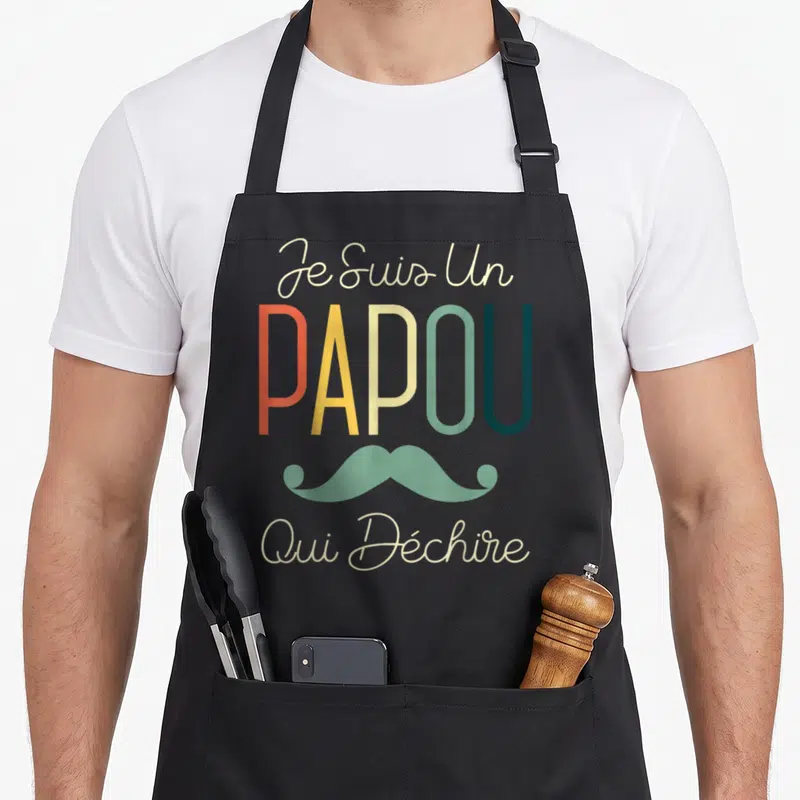 Tablier de cuisine noir avec le texte Je Suis Un Papou Qui Déchire et une illustration de moustache verte.
