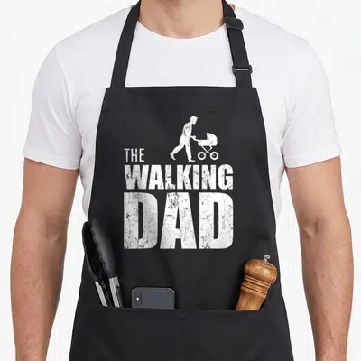 Tablier de cuisine noir avec le texte The Walking Dad et une silhouette blanche poussant une poussette.