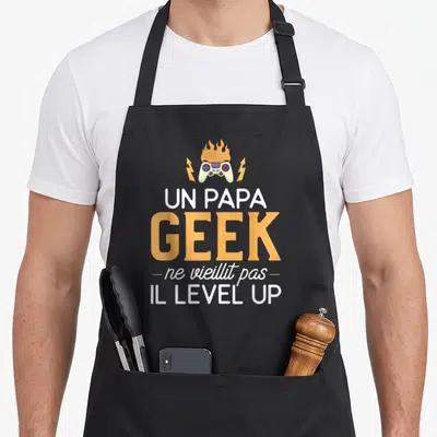 Tablier de cuisine noir avec manette de jeu en feu et texte un papa geek ne vieillit pas il level up