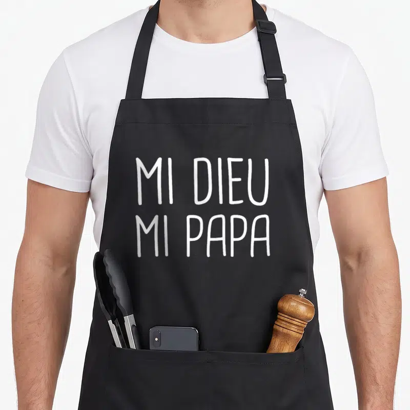 Tablier de cuisine noir avec l'inscription blanche mi dieu mi papa en lettres capitales manuscrites.
