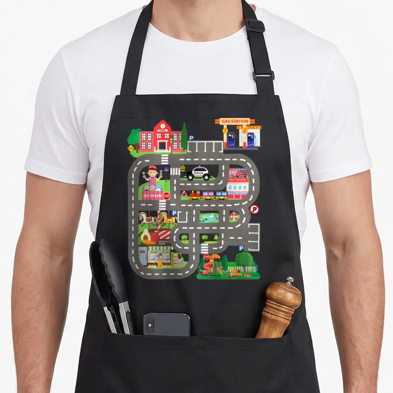 Tablier de cuisine noir avec circuit de course coloré incluant une police, une caserne de pompiers et une école.