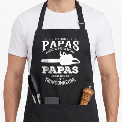 Tablier de cuisine noir avec silhouette blanche de tronçonneuse et texte certain papas jouent avec une tronçonneuse