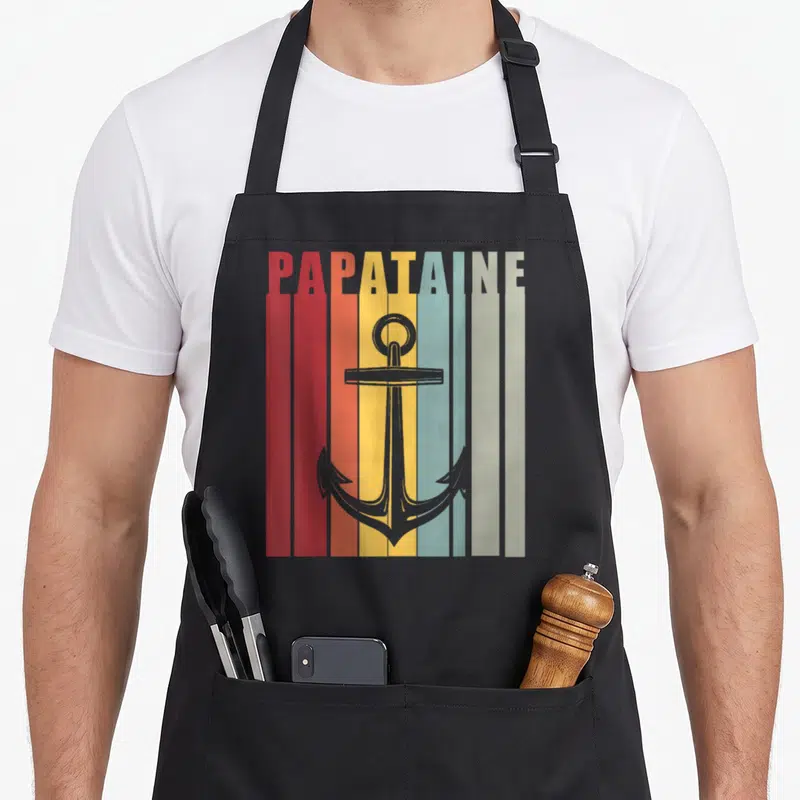 Tablier de cuisine noir avec inscription Papataine et illustration d'ancre sur bandes colorées verticales.