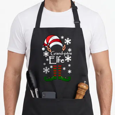 Tablier de cuisine noir avec illustration de chapeau et bottes d'elfe, texte Grand-père Elfe et flocons de neige blancs.