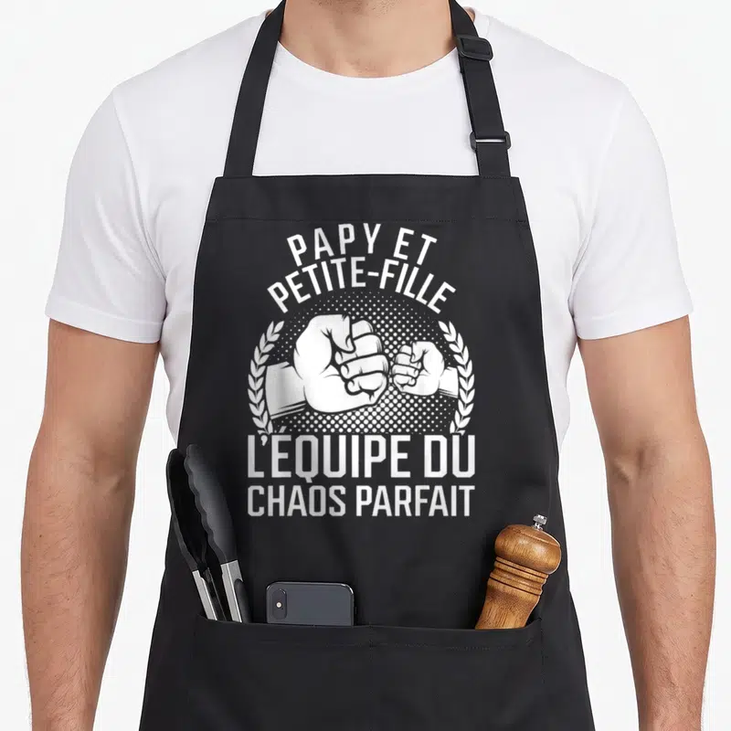Tablier de cuisine noir avec une illustration blanche de deux poings se touchant et le texte Papy et Petite-Fille L'équipe du chaos parfait.