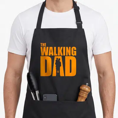 Tablier de cuisine noir avec le texte The Walking Dad en orange et une silhouette de père portant un enfant dans la lettre A.