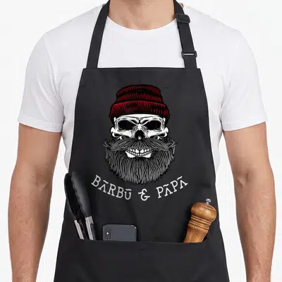 Tablier de cuisine noir avec illustration d'un crâne barbu portant une bonnette rouge et le texte Barbu & Papa.