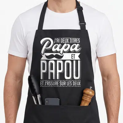Tablier de cuisine noir avec inscription blanche J'ai deux titres Papa et Papou et moustache stylisée.